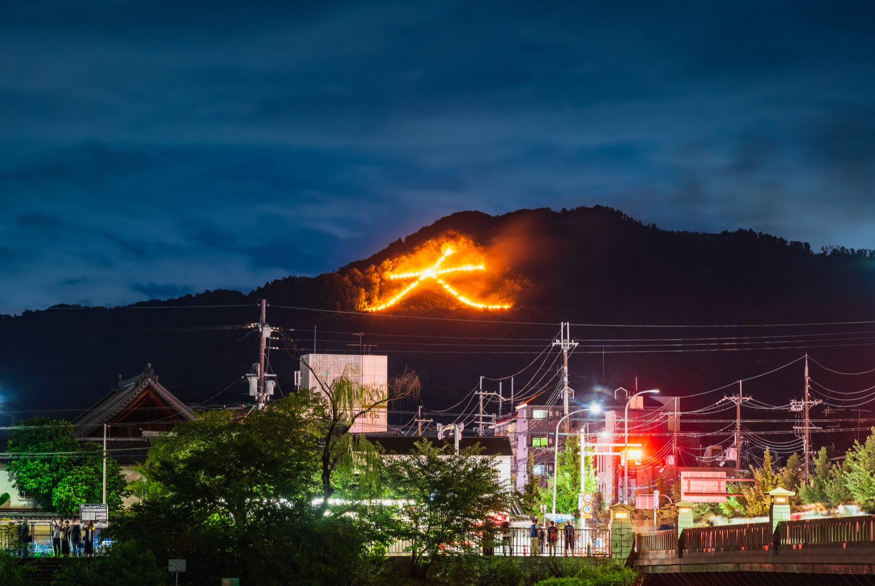 The giant burning dai character of the Daimonji Gozan no Okuribi bonfire glowing orange on a dark forested hillside above Kyoto at night on August 16, with the lit town below