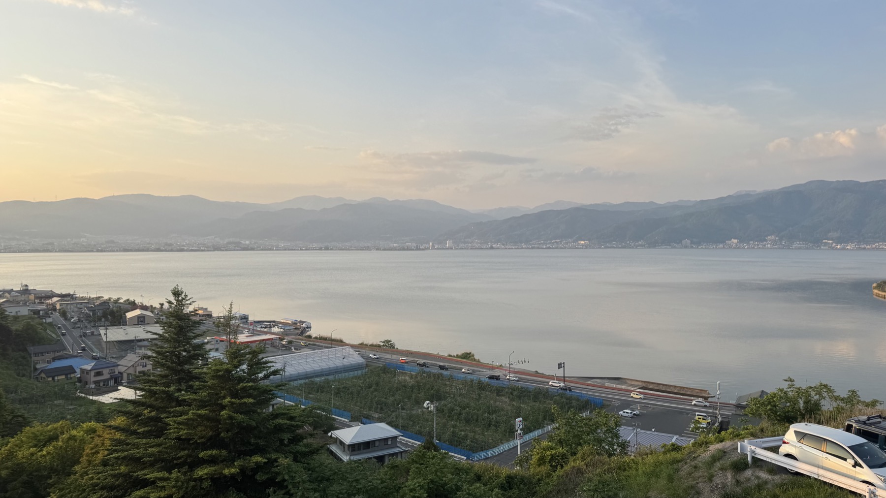 Calm Lake Suwa at dusk with a small boat moored in the foreground and soft pastel light over the mountains on the far side of the lake.