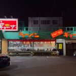 The Nankintei Kunitachi branch lit up at night, a green-roofed roadside Chinese diner with glowing red ramen and gyoza signs, a 24-hour notice and a wide car park out front in Kunitachi, Tokyo.