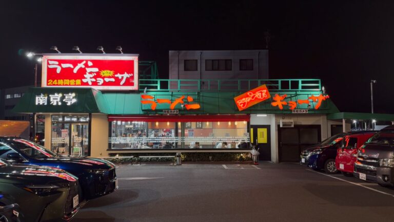 The Nankintei Kunitachi branch lit up at night, a green-roofed roadside Chinese diner with glowing red ramen and gyoza signs, a 24-hour notice and a wide car park out front in Kunitachi, Tokyo.