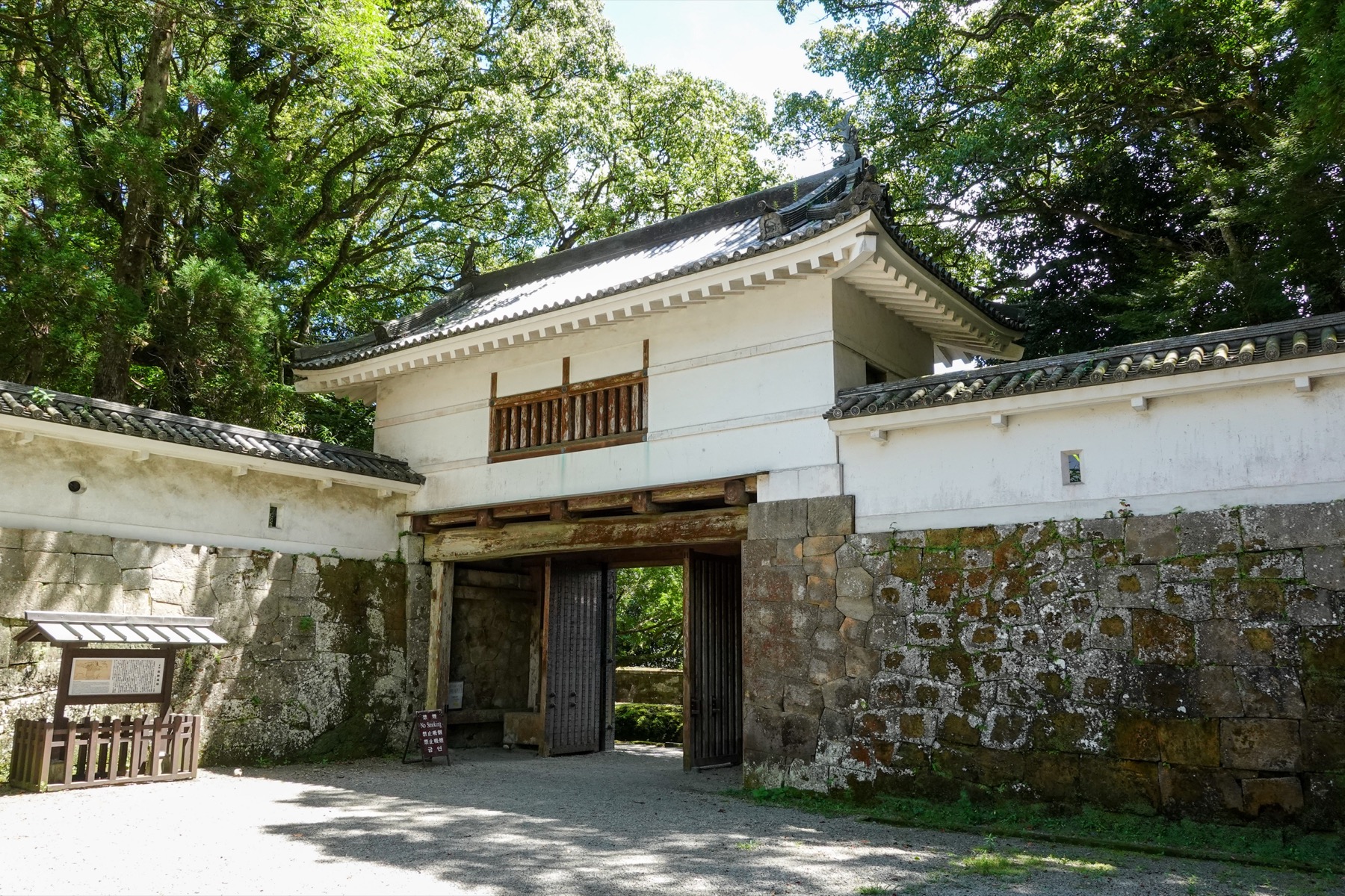 A white-plastered turret gate set into the massive rusticated stone ramparts of Obi Castle, built from the area's distinctive porous Obi stone, with an information board and steps leading through the gateway.