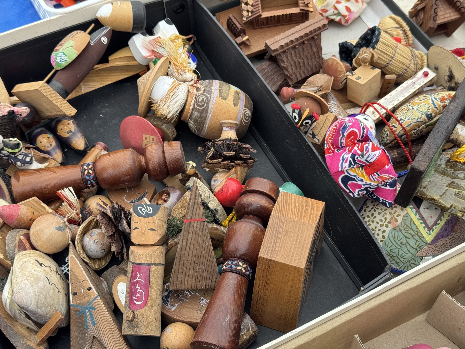 Boxes of small wooden folk crafts, kokeshi dolls and Showa-era curios for sale at the Ōi Racecourse flea market in Tokyo.