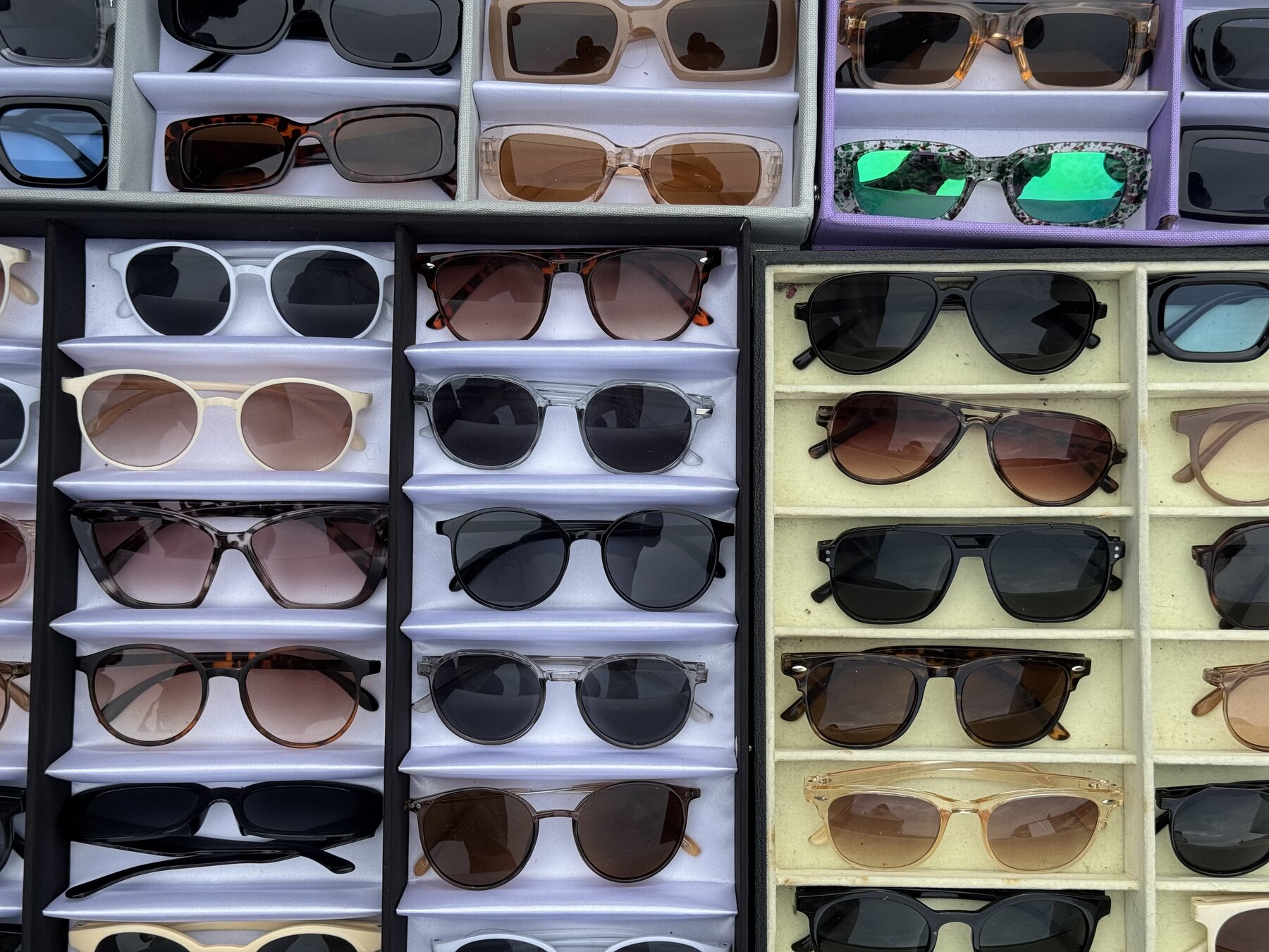 Trays of dozens of second-hand and vintage sunglasses in various frame styles displayed at a stall at the Ōi Racecourse flea market in Tokyo.