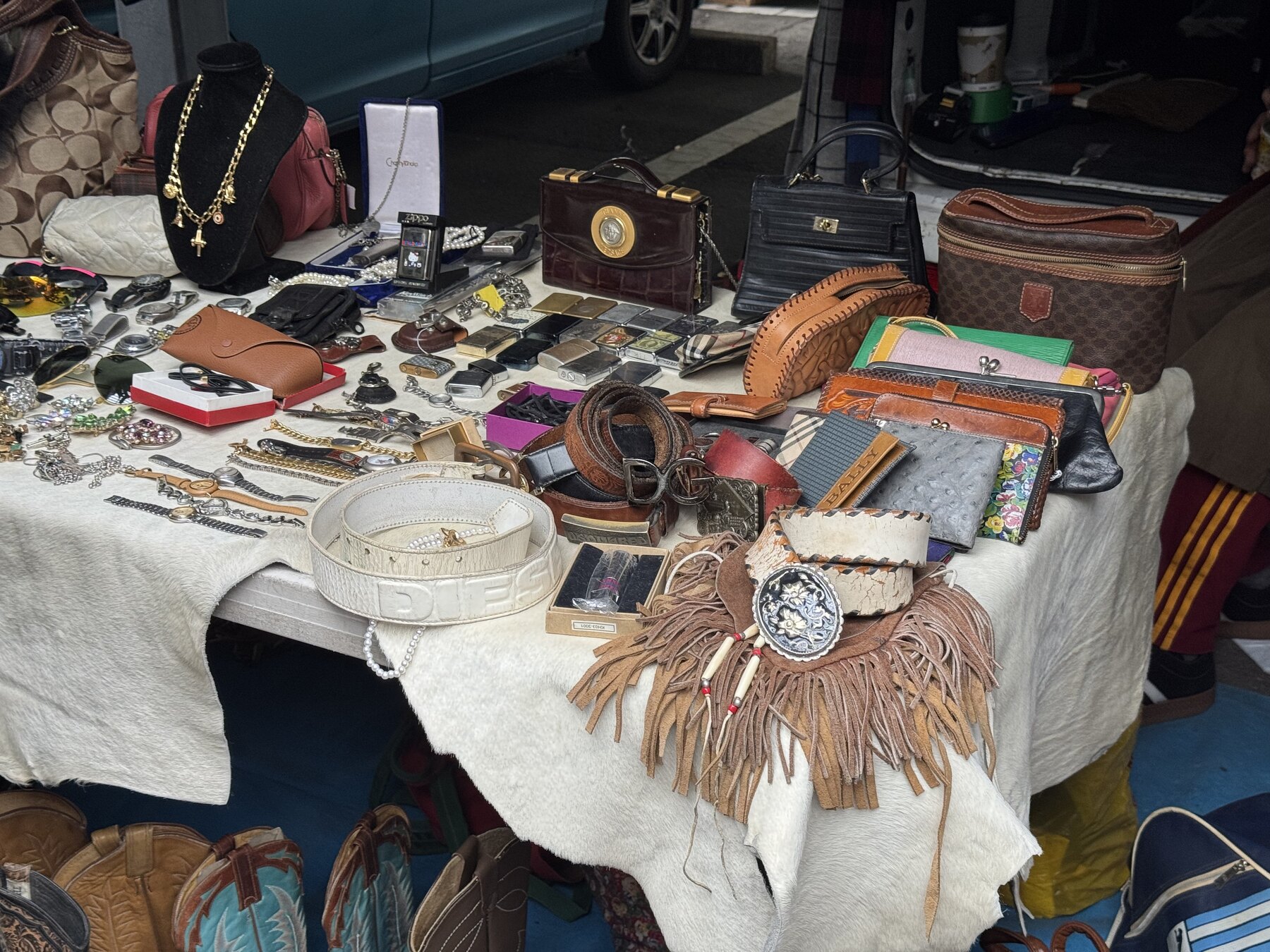 A stall table at the Ōi Racecourse flea market spread with vintage leather bags, wallets, belts, watches and jewellery laid out on a cloth.