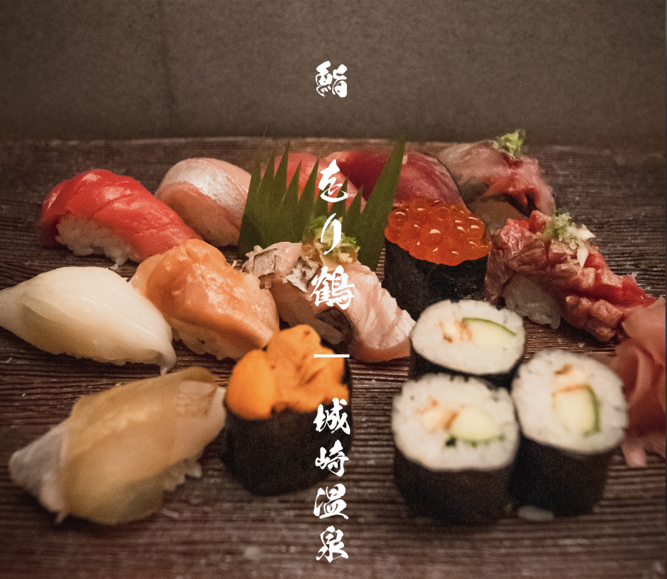 A wide assortment of nigiri, gunkan, and maki sushi arranged on a dark wooden board at Orizuru in Kinosaki Onsen, with vertical white Japanese lettering reading Sushi Orizuru Kinosaki Onsen.