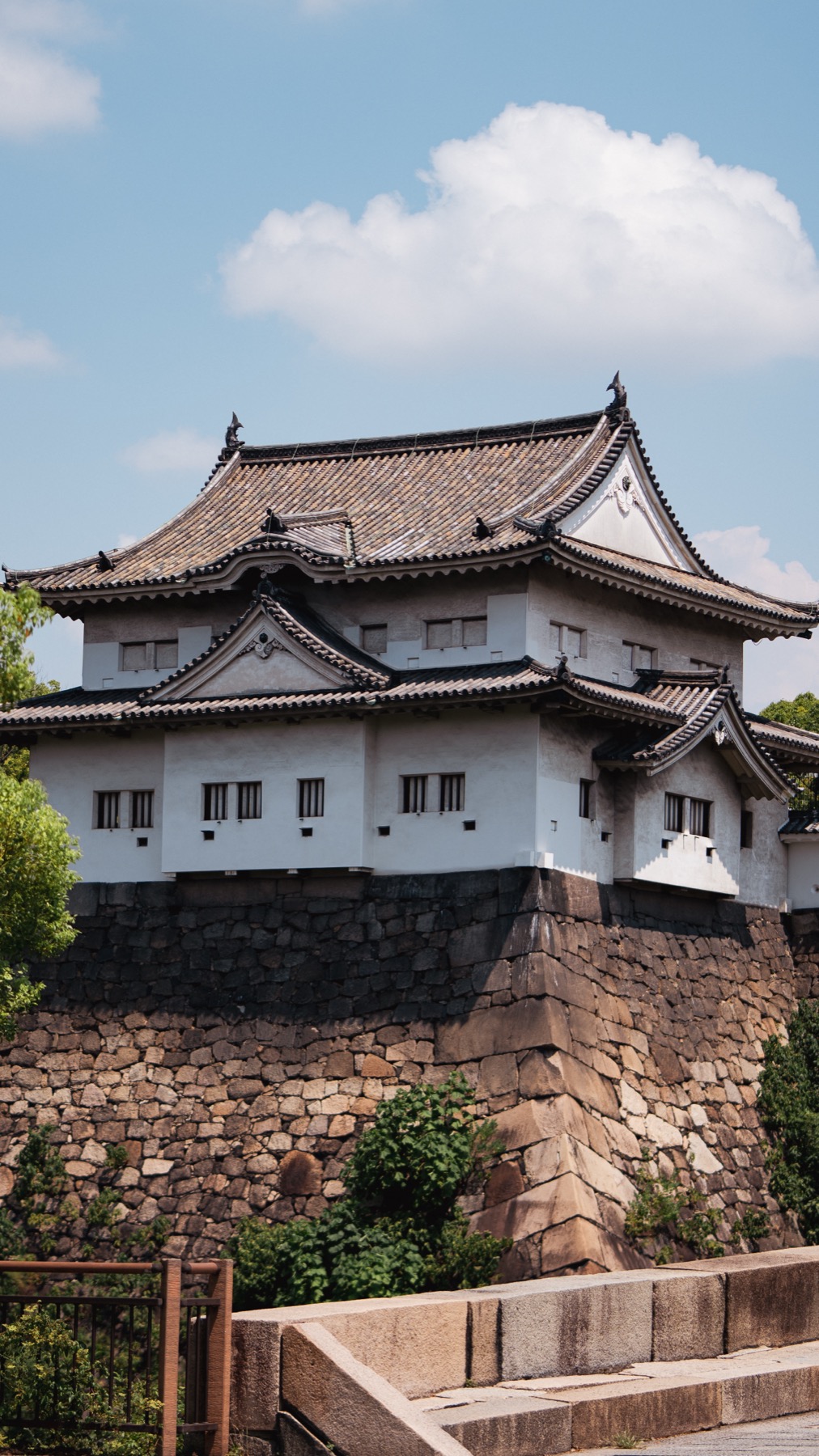 A surviving Edo-period turret of Osaka Castle, a white multi-storey yagura with tiled eaves standing on a steep base of fitted stone blocks, designated an Important Cultural Property, against a blue sky.