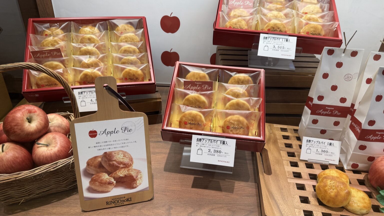 Boxed apple pies on display at Ringo no Ki patisserie in Chikuma, Nagano, beside a basket of red apples and gift bags printed with apples, price cards in front
