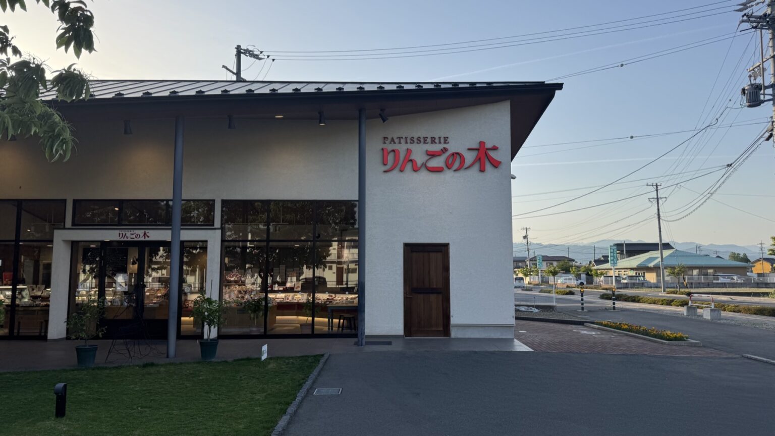 The clean white modern exterior of Patisserie Ringo no Ki in Chikuma, Nagano, with red lettering and large windows showing the cake cases inside at dusk