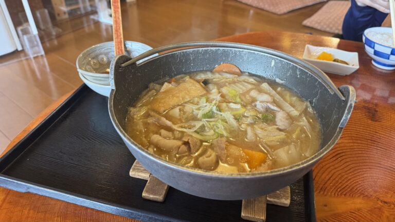 A black iron pot of pork hoto at Shoya by Lake Yamanaka: flat, wide wheat noodles simmered with pork, pumpkin and vegetables in a thick miso broth, on a wooden tray with rice and pickles