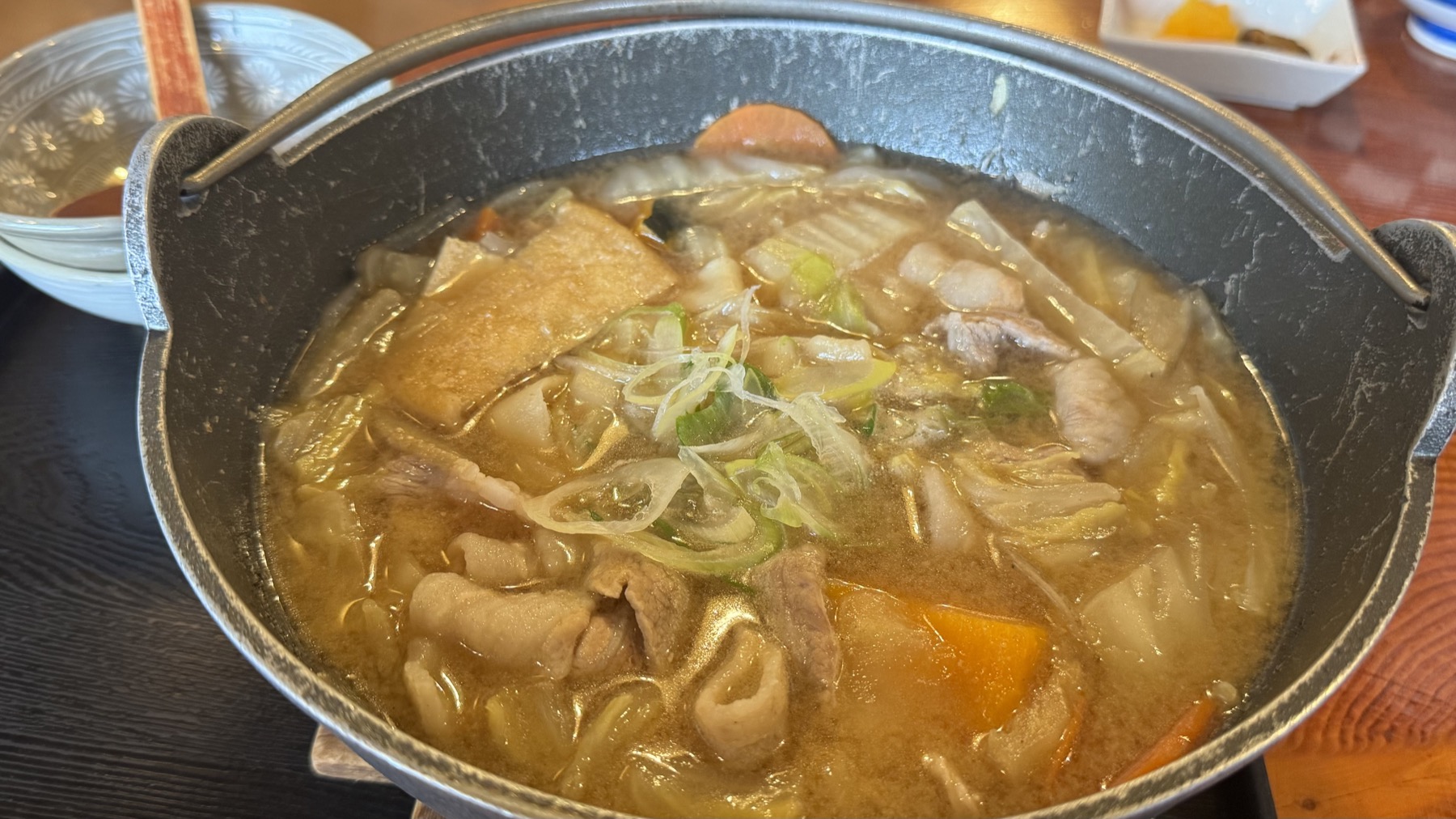 A close view into the iron pot of pork hoto at Shoya, the thick miso broth dense with wide flat noodles, sliced pork, leek and root vegetables