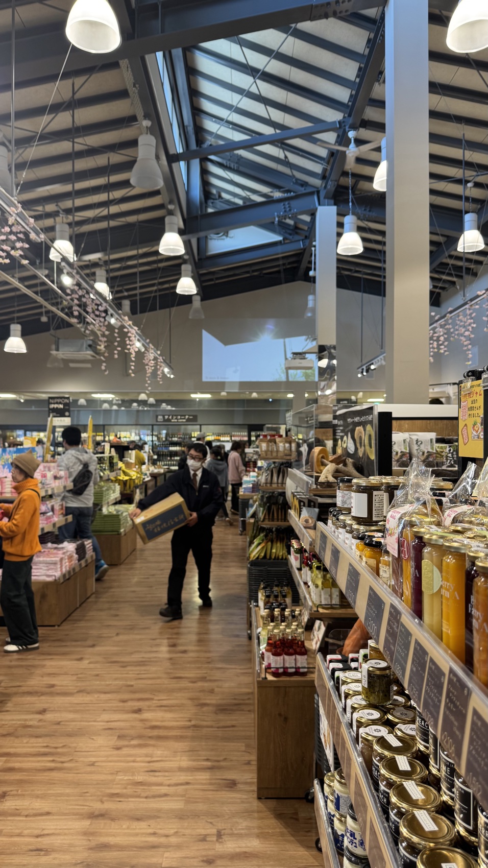 Shoppers browsing a wide market aisle stocked with local food products at the Asama Market, Tabi-no-Eki Kawaguchiko Base.