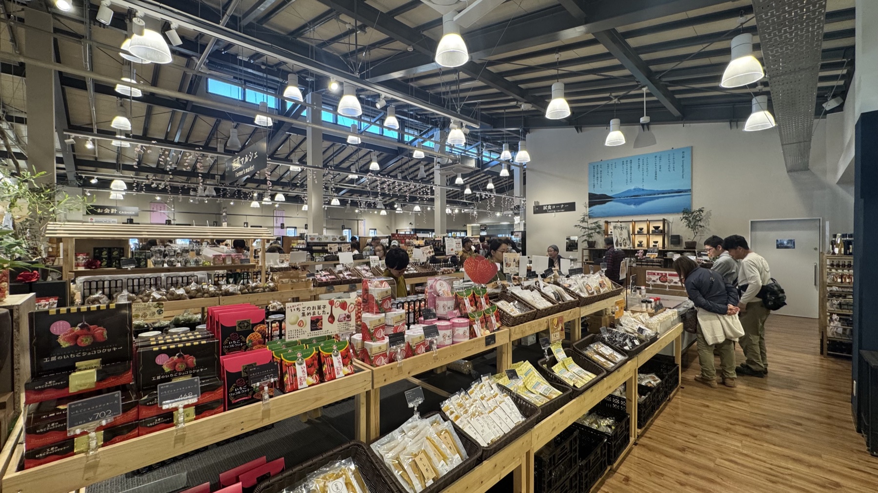 The Asama Market food hall at Tabi-no-Eki Kawaguchiko Base, with wooden display tables of local sweets and products under pendant lights and a Mt Fuji photo on the wall.
