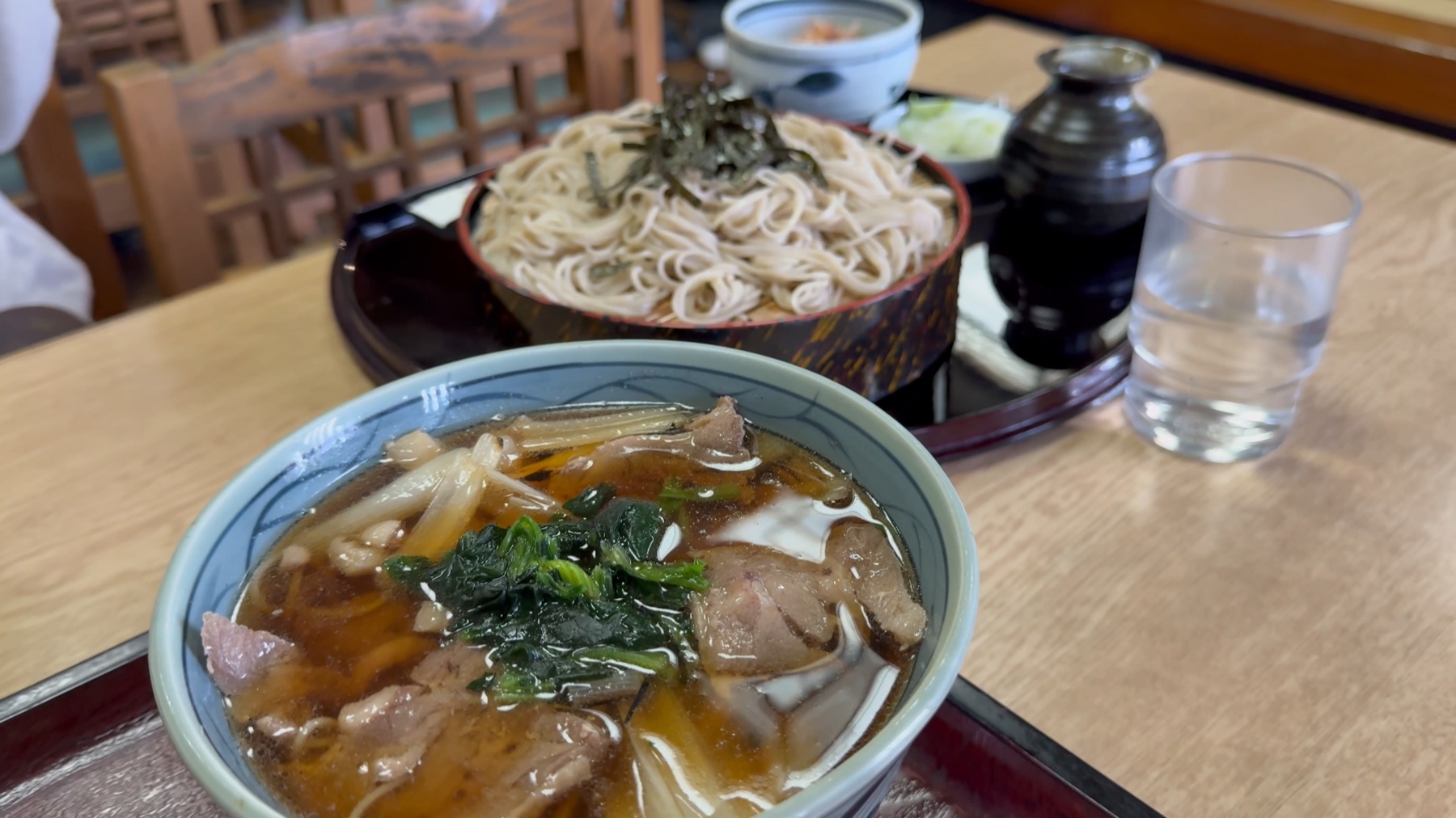 Close-up of the hot duck-and-leek dipping broth at Takinoya, with sliced duck, leek and greens, beside a tray of chilled soba and a glass of water.