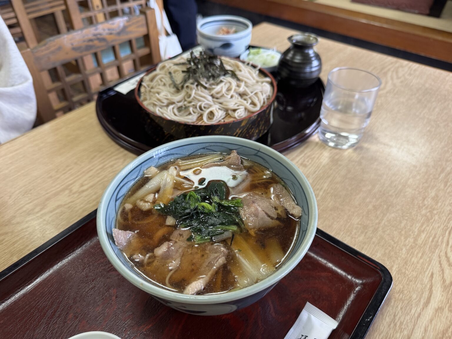 A duck soba set at Takinoya in Mitaka: a bowl of hot duck-and-leek dipping broth in the front and a tray of chilled soba noodles behind, with condiments, on a wood table.