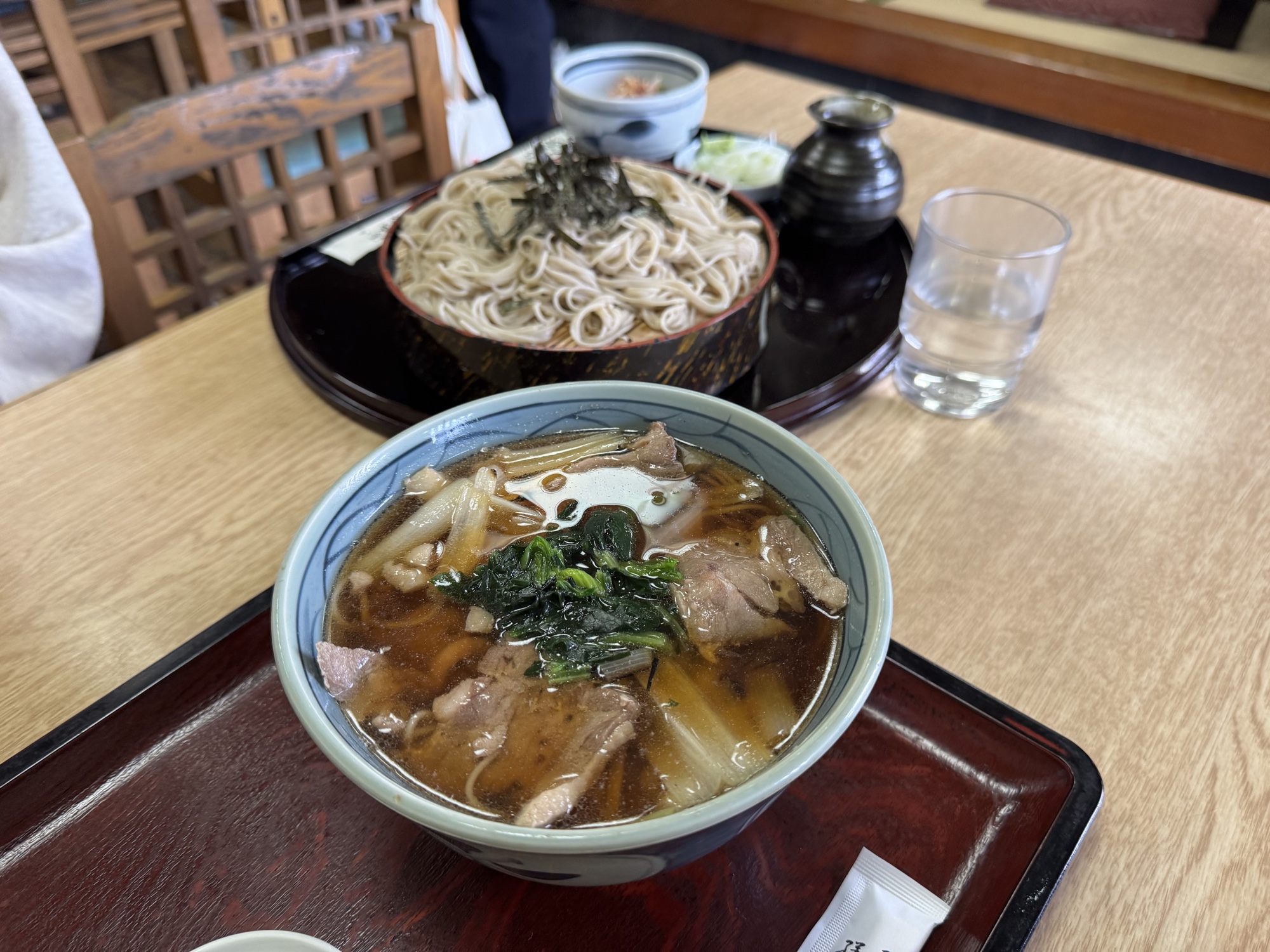 A duck soba set at Takinoya in Mitaka: a bowl of hot duck-and-leek dipping broth in the front and a tray of chilled soba noodles behind, with condiments, on a wood table.