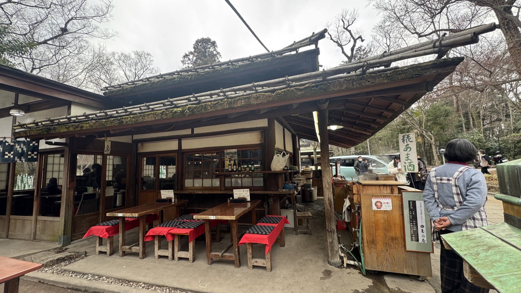 The rustic wooden exterior of Tamanoya soba house in Jindaiji, Chofu, with outdoor bench seating and a low roof set among green trees near the Jindai Botanical Gardens