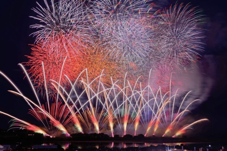 A wide star-mine of red, orange and silver fireworks fills the night sky and reflects across the dark surface of the Tone River at the Sakai Grand Fireworks festival in Ibaraki, Japan.