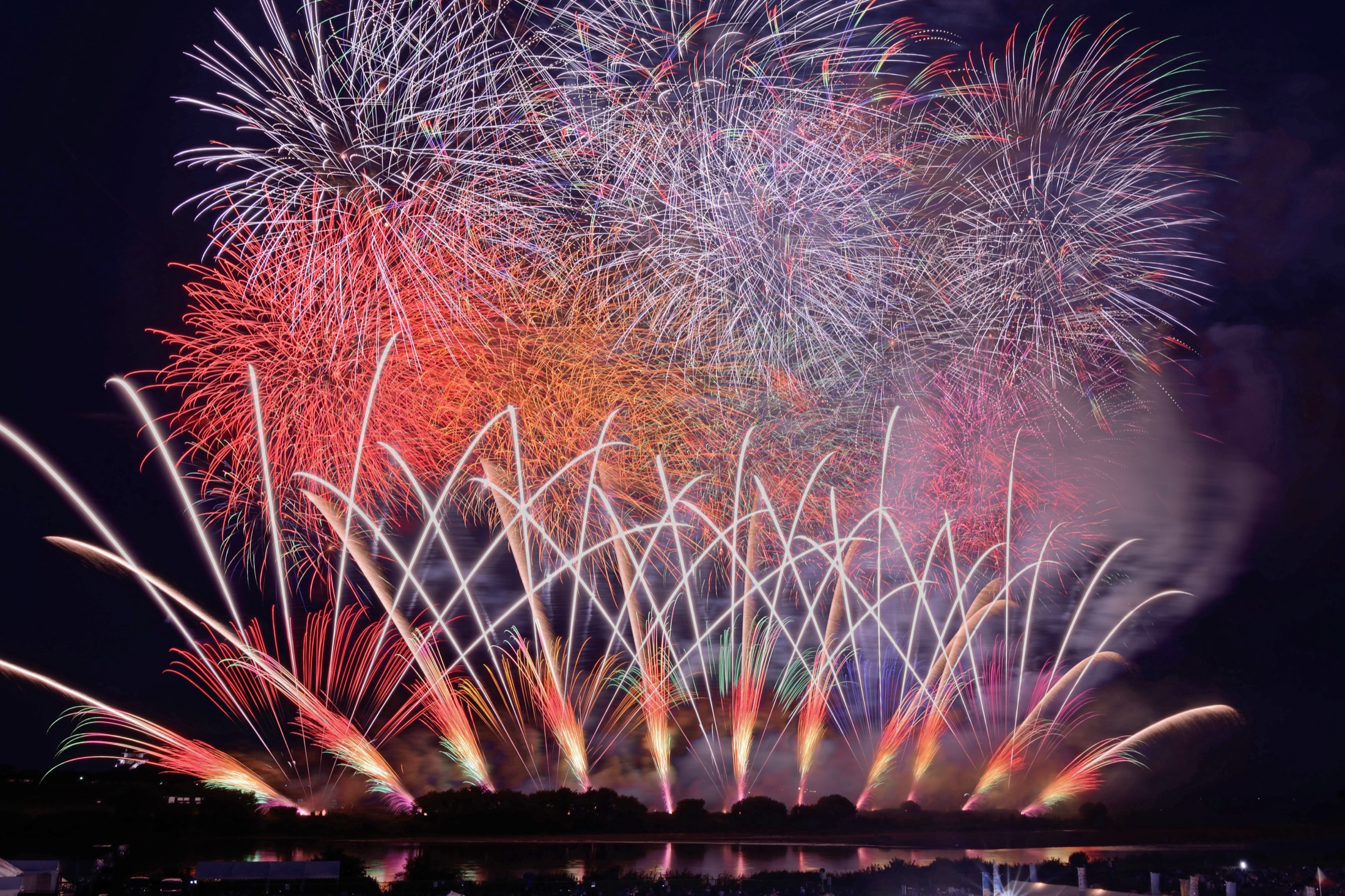 A wide star-mine of red, orange and silver fireworks fills the night sky and reflects across the dark surface of the Tone River at the Sakai Grand Fireworks festival in Ibaraki, Japan.