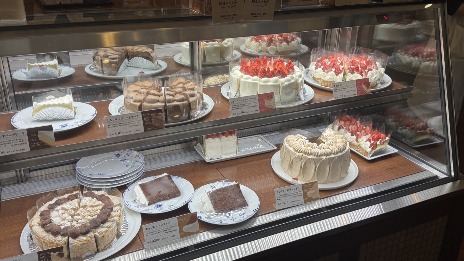 The cake counter at Tsubakiya Cafe Kichijoji, a refrigerated glass case full of whole cakes including strawberry shortcake, chocolate cake and mont blanc with price cards, available to eat in or take home
