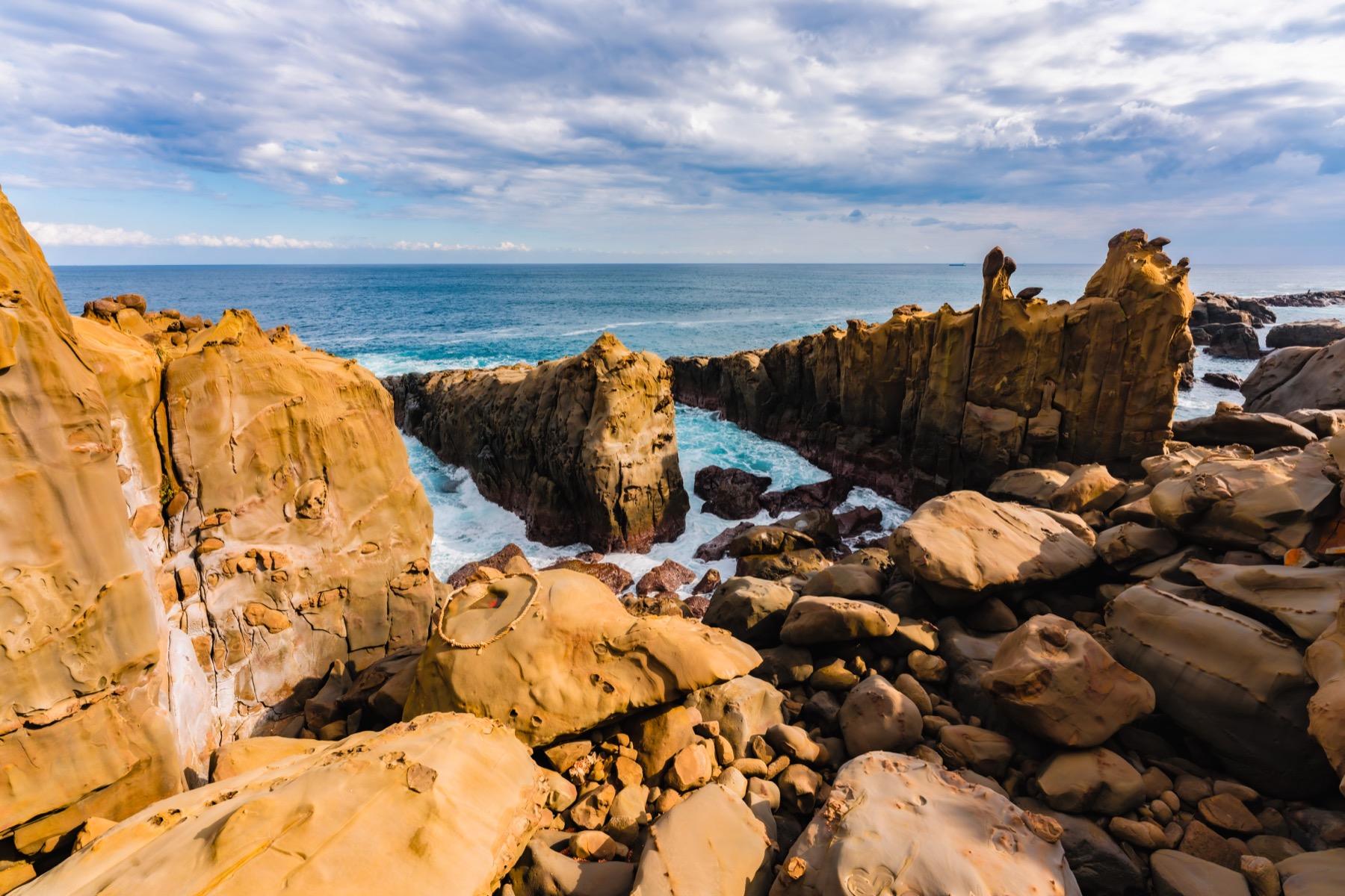 The dramatic sandstone rock formations and surf of the Hyuga-nada coast around Udo Jingu in Nichinan, Miyazaki, under a cloudy blue sky.