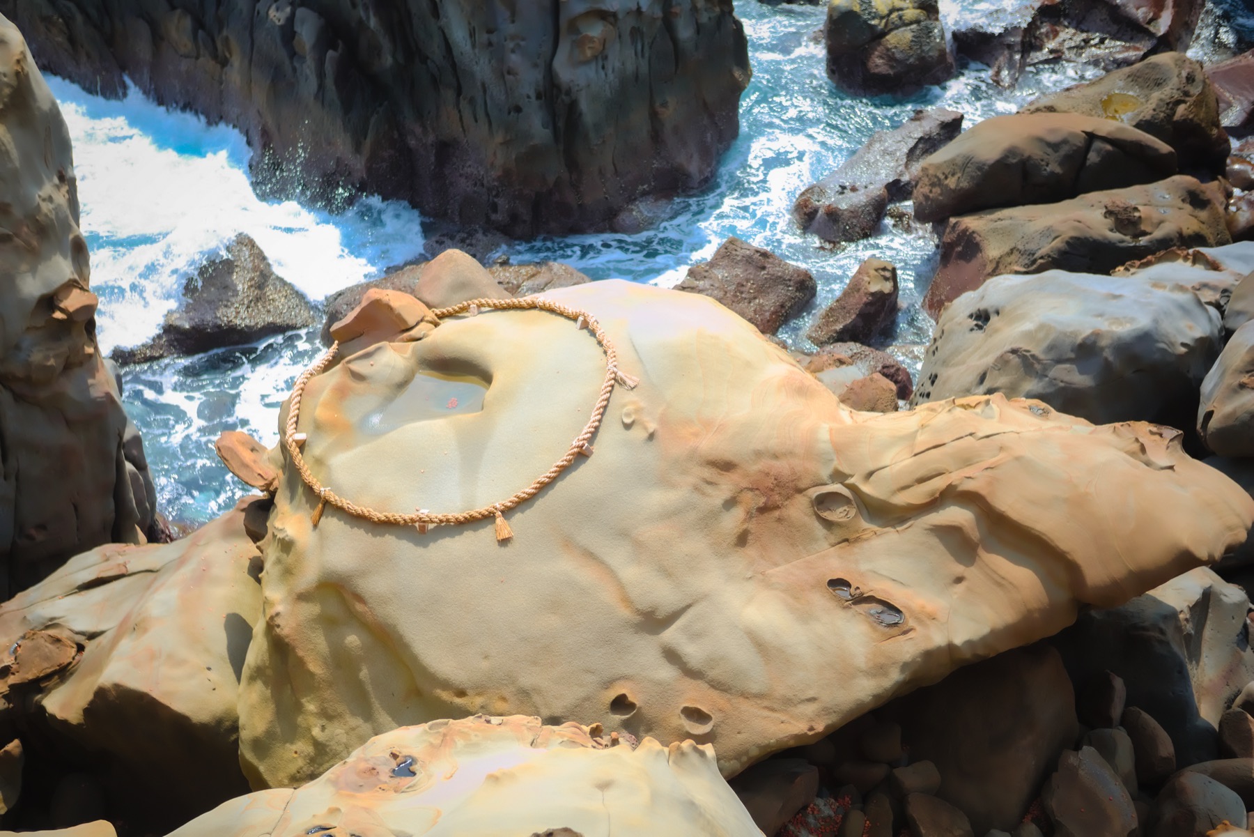 The turtle-shaped rock at Udo Jingu with a rope-ringed hollow on top, the target for tossing undama lucky clay balls, waves breaking on the rocks below in Miyazaki.