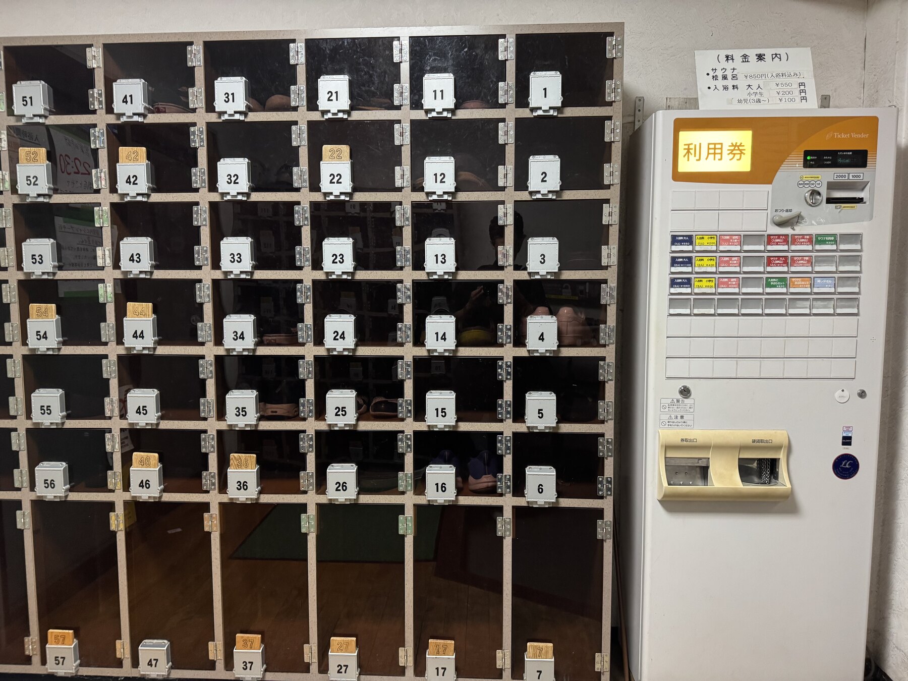 The entrance of Ume-no-Yu with numbered wooden shoe lockers and a ticket vending machine showing the bathing fees.