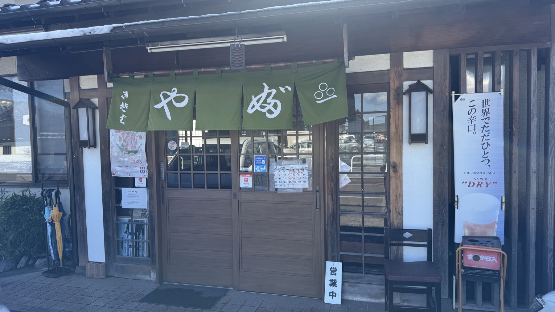 The traditional wooden storefront of Oshokuji-dokoro Yabu in Fujiyoshida, with a green noren curtain reading Yabu, an open sign and lanterns by the sliding entrance