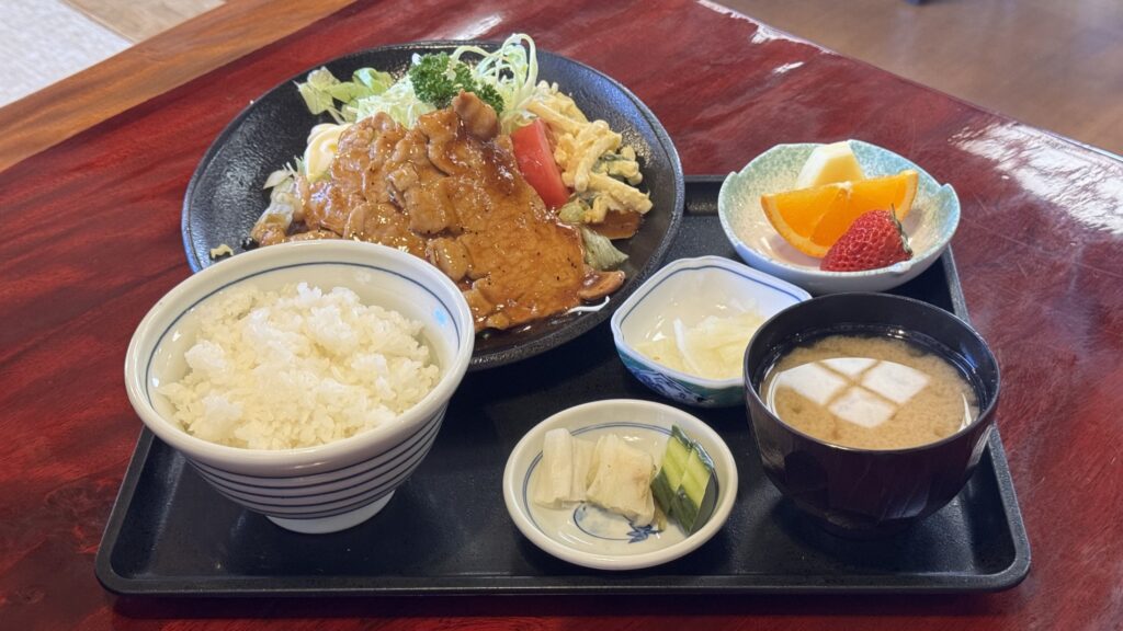 A ginger-pork set meal at Yabu in Fujiyoshida: glazed shogayaki pork with shredded cabbage and scrambled egg, a bowl of rice, miso soup, pickles and a small dish of fresh fruit on a black tray