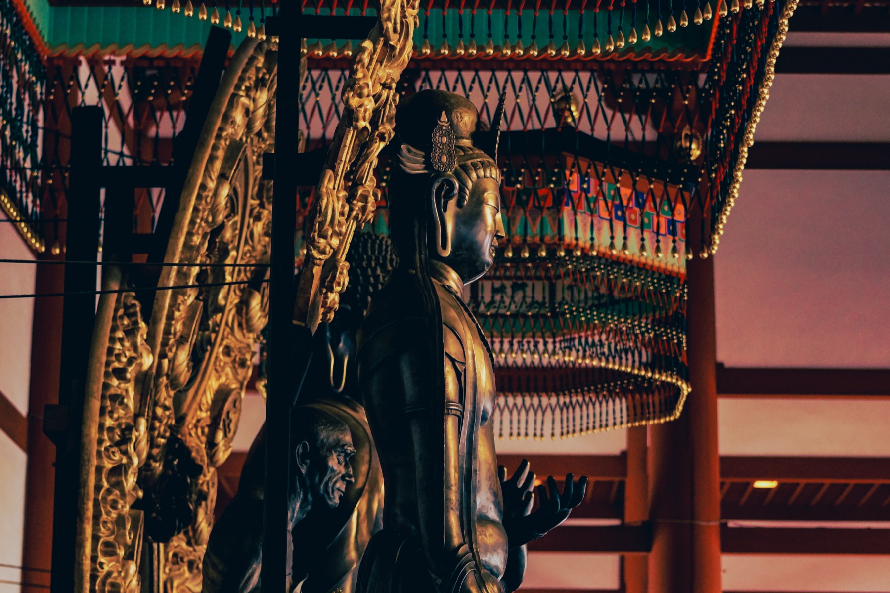 A dark bronze bodhisattva statue with a flaming halo beneath an ornate gilt canopy inside a hall at Yakushiji Temple in Nara, one of the temple celebrated Hakuho-era bronze sculptures.