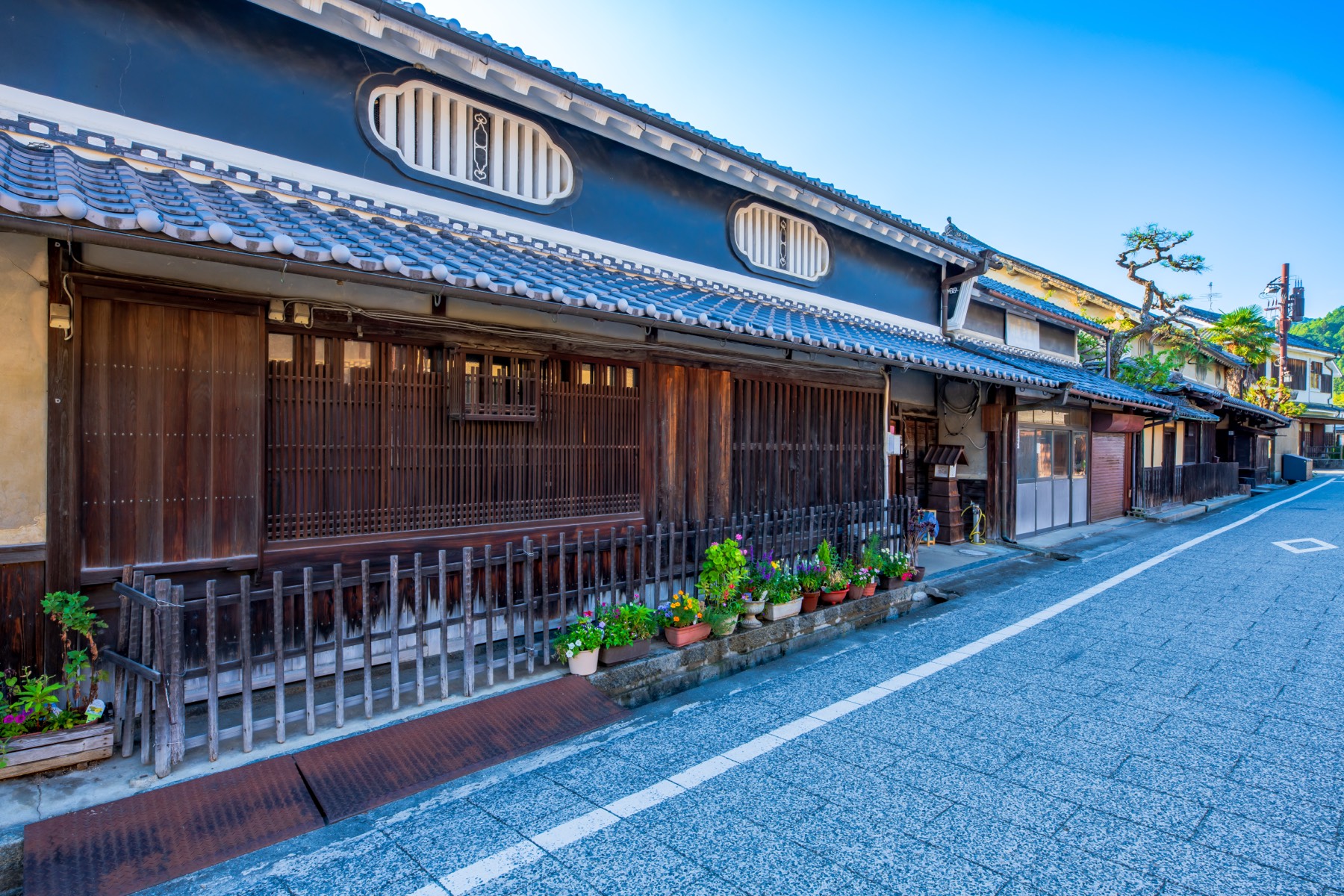 The long wooden-lattice frontage of a preserved traditional house in the Oka townscape of Asuka village with white-plaster upper wall and potted plants along the street