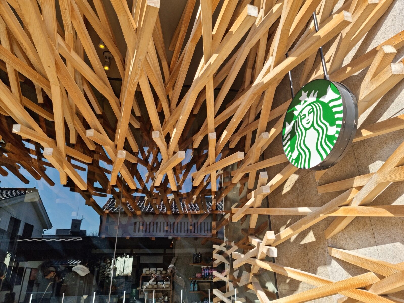 Close-up of the diagonal cedar battens and the Starbucks logo at the Dazaifu Tenmangu Omotesando store, with a traditional building reflected in the glass
