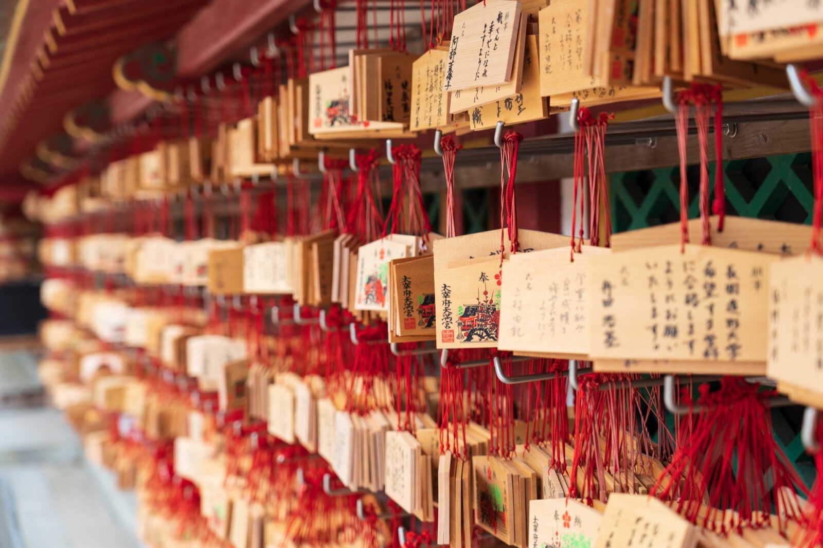 Rows of wooden ema prayer plaques hung with red cords at Dazaifu Tenmangu, many carrying wishes for success in school and university exams