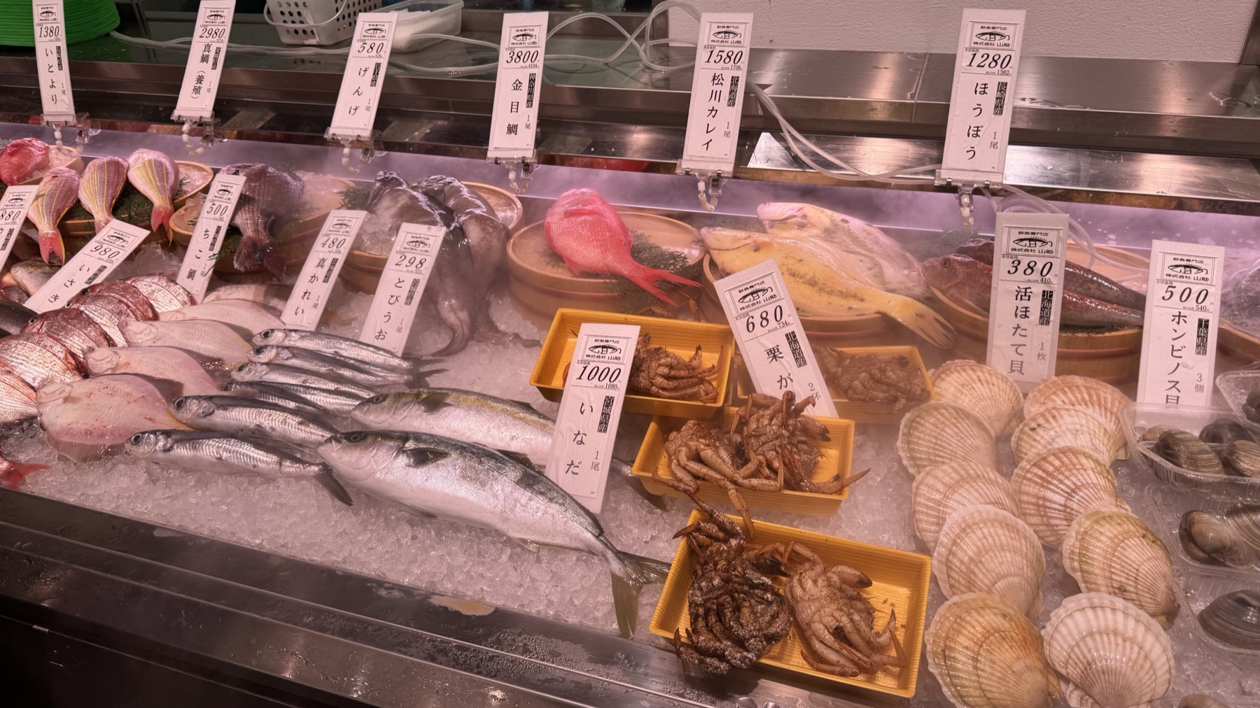 A fresh fish counter run by Yamausuke at Farmers Gotemba with whole kinmedai, flatfish, scallops and clams on ice with price tags in Gotemba