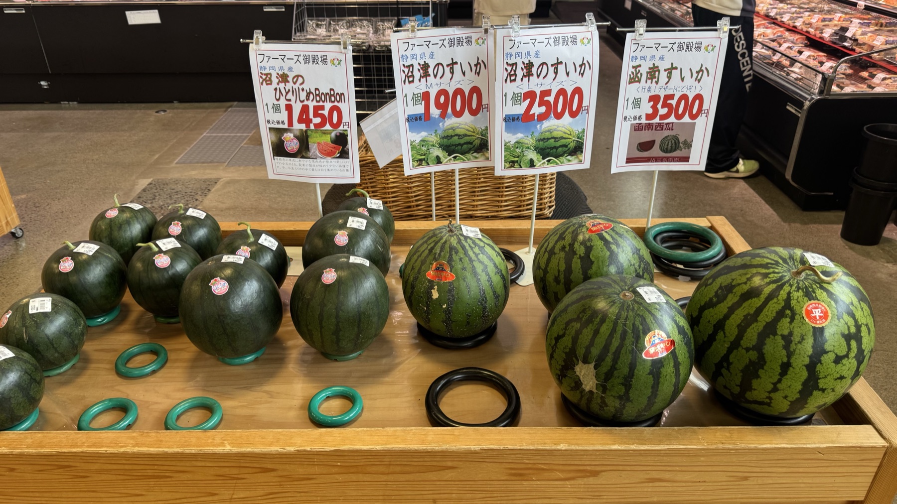 Round Numazu and Kannami brand watermelons on a wooden display with price signs from 1,450 to 3,500 yen at Farmers Gotemba market in Shizuoka