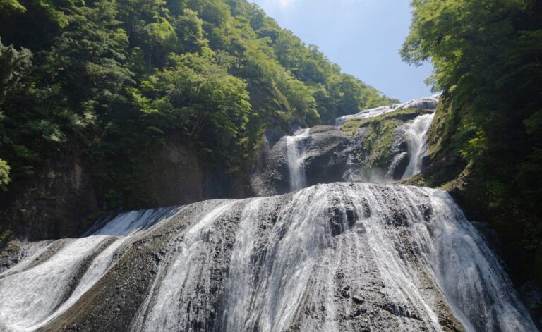 Fukuroda Falls in Ibaraki cascading 120 metres down four broad rock tiers surrounded by deep green summer forest under a blue sky