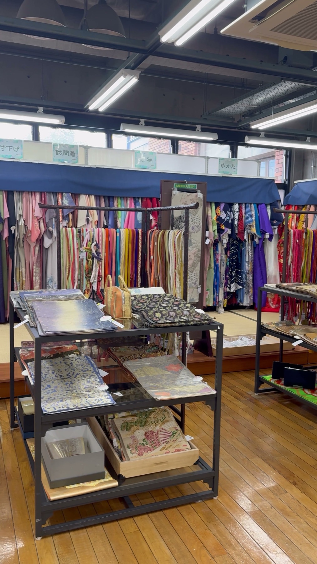 Racks of secondhand kimono labelled by type with tsukesage, houmongi and yukata sections and a glass case of obi in the large used kimono department at Off House Hachioji Owada, Tokyo