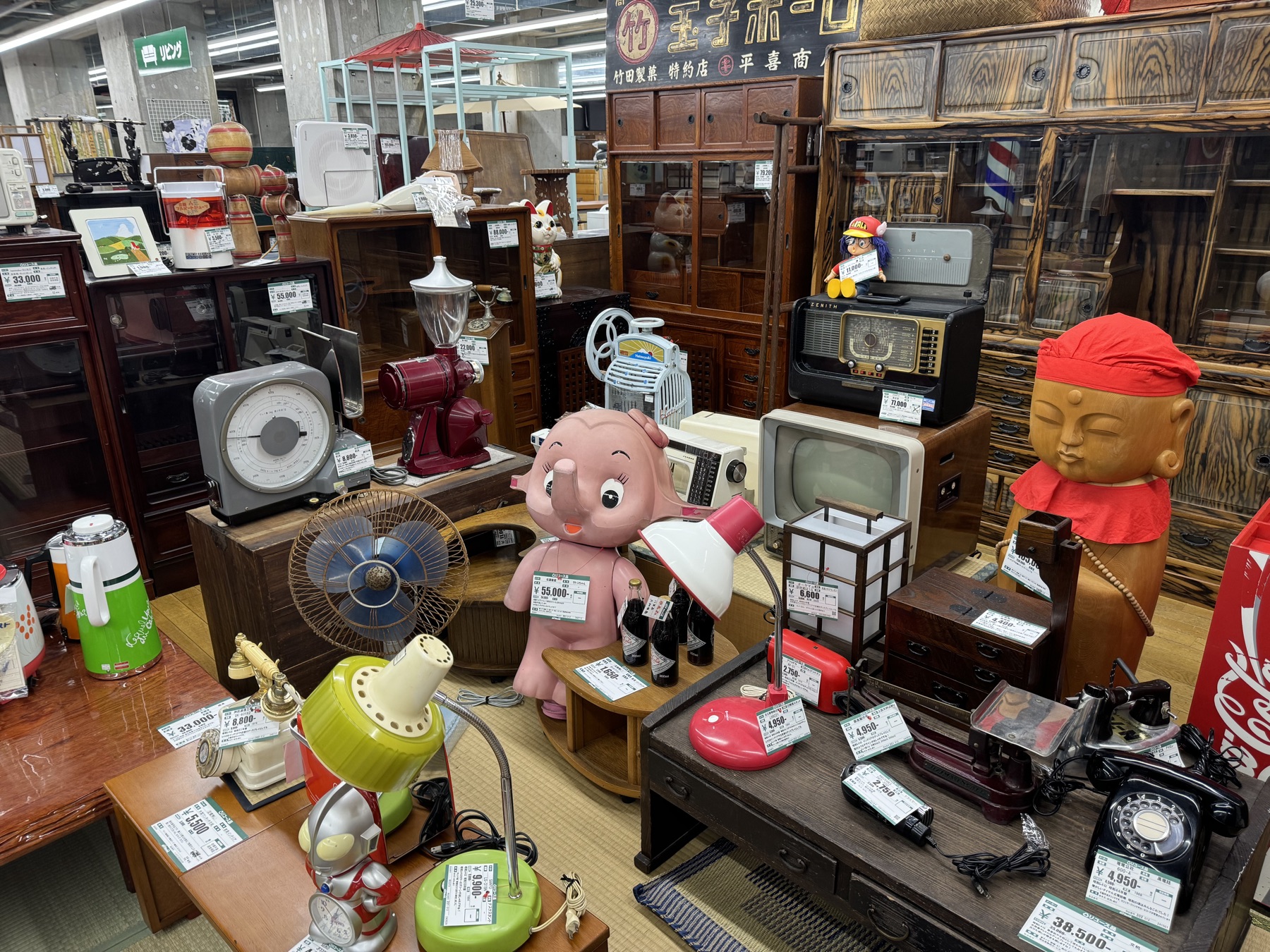A Showa era retro corner with vintage electric fans, an old boxy television, black rotary telephones, a pink elephant lamp and an enamel shop sign at Off House Hachioji Owada, Tokyo