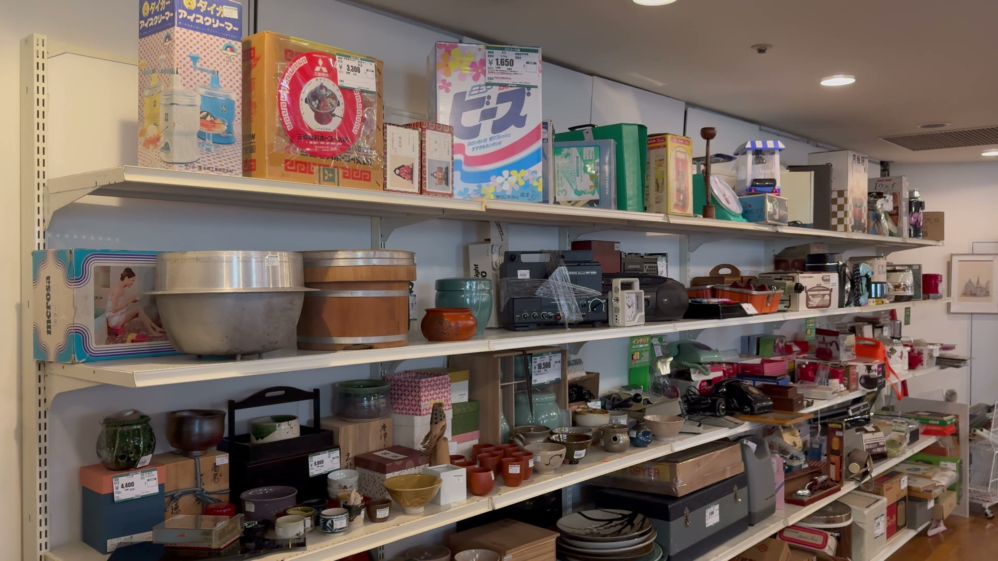 Shelves of Showa era retro goods including vintage packaged items, an aluminium rice tub, old radios and ceramics in the retro corner at Off House Hachioji Owada, Tokyo