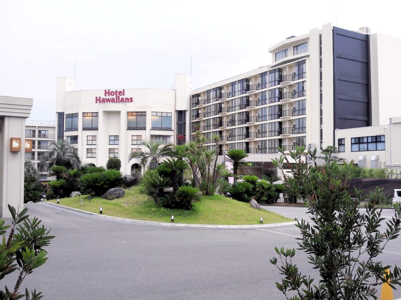 The exterior of Hotel Hawaiians, a white multi-storey hotel with the Hotel Hawaiians sign, palm trees and a landscaped driveway