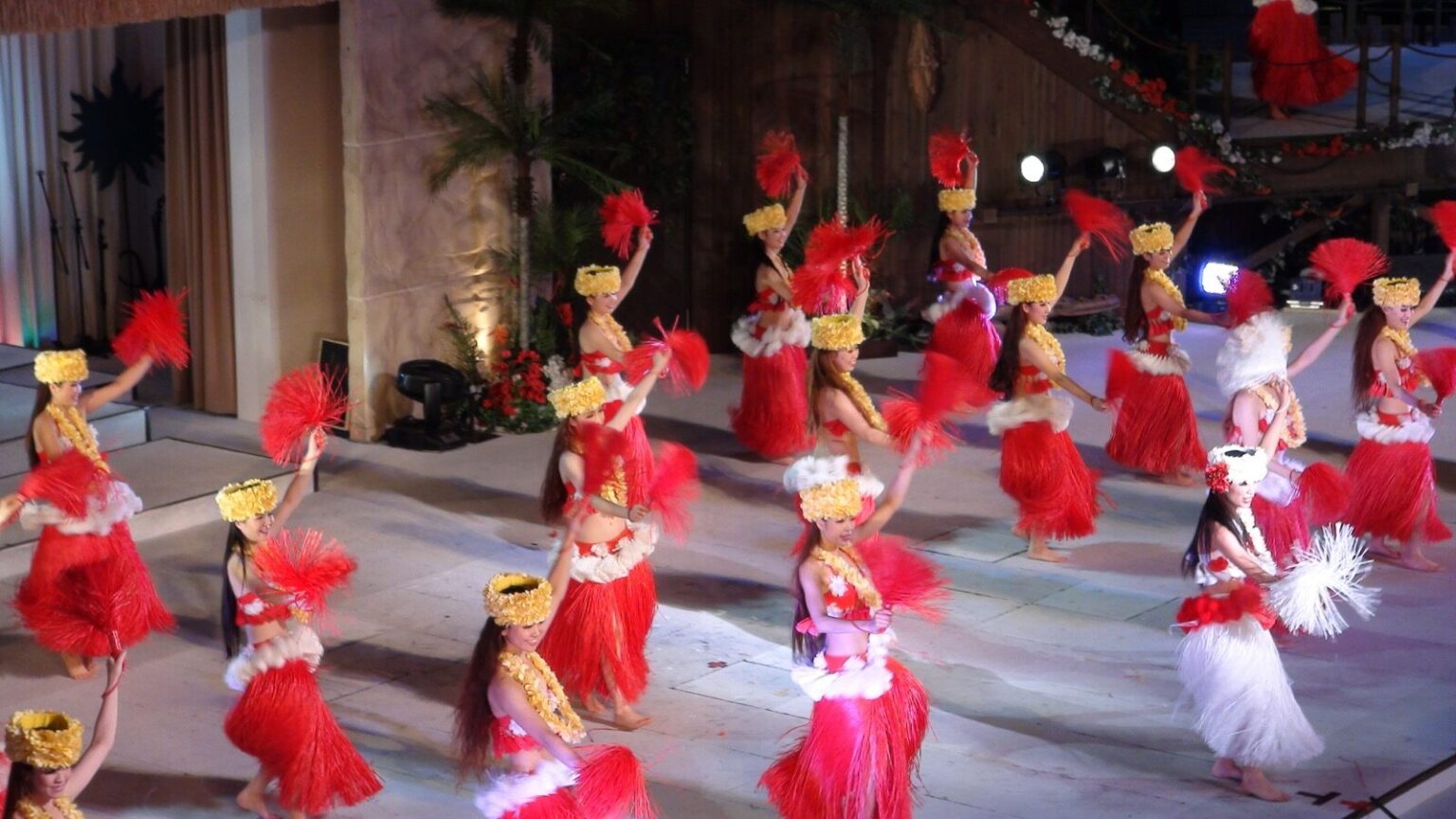 Rows of dancers in red-and-white hula costumes and headpieces performing the Polynesian show on stage at Spa Resort Hawaiians
