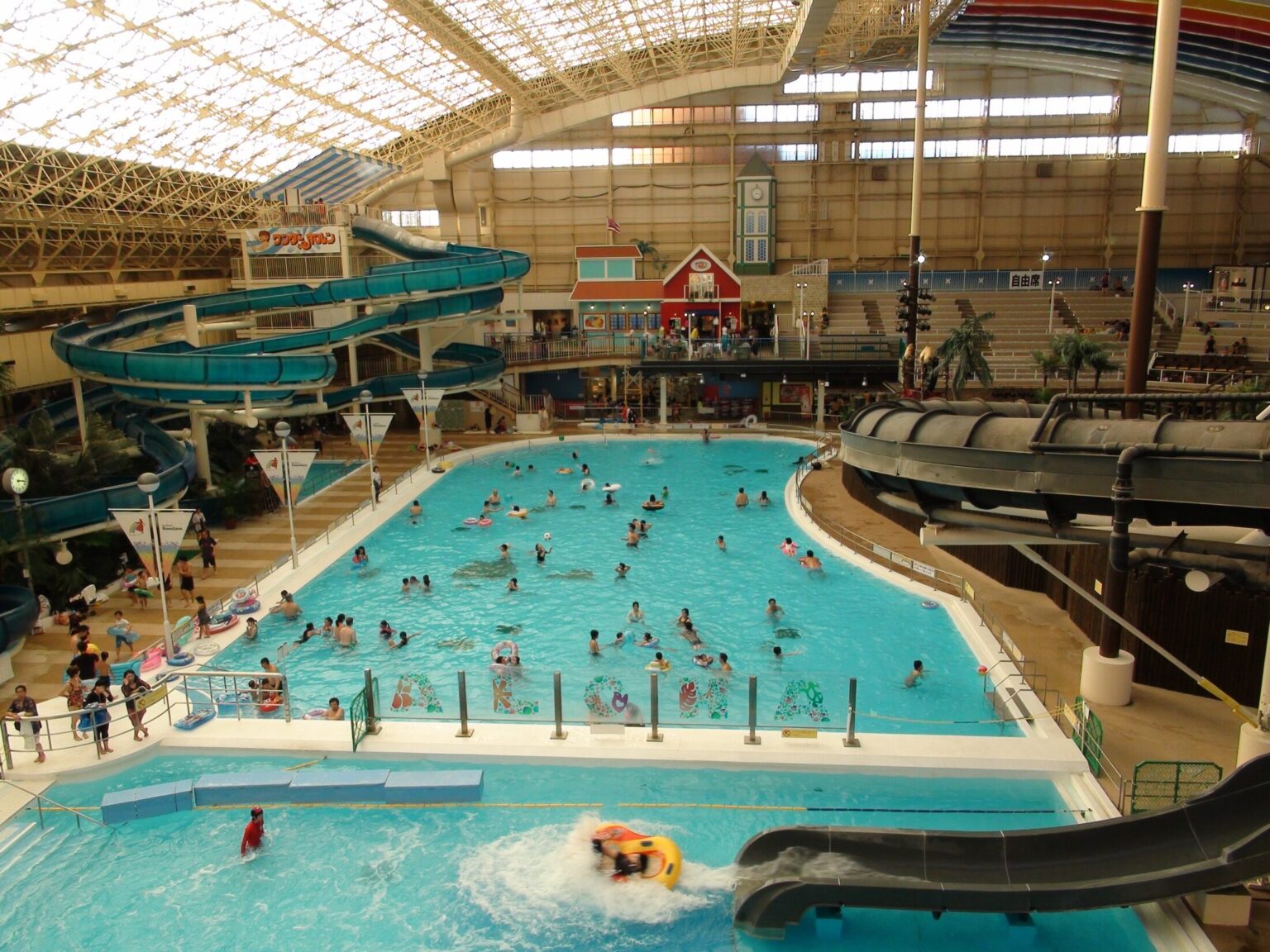 The vast domed indoor Water Park at Spa Resort Hawaiians with a large blue wave pool, water slides, palm trees and a curved glass-and-steel roof