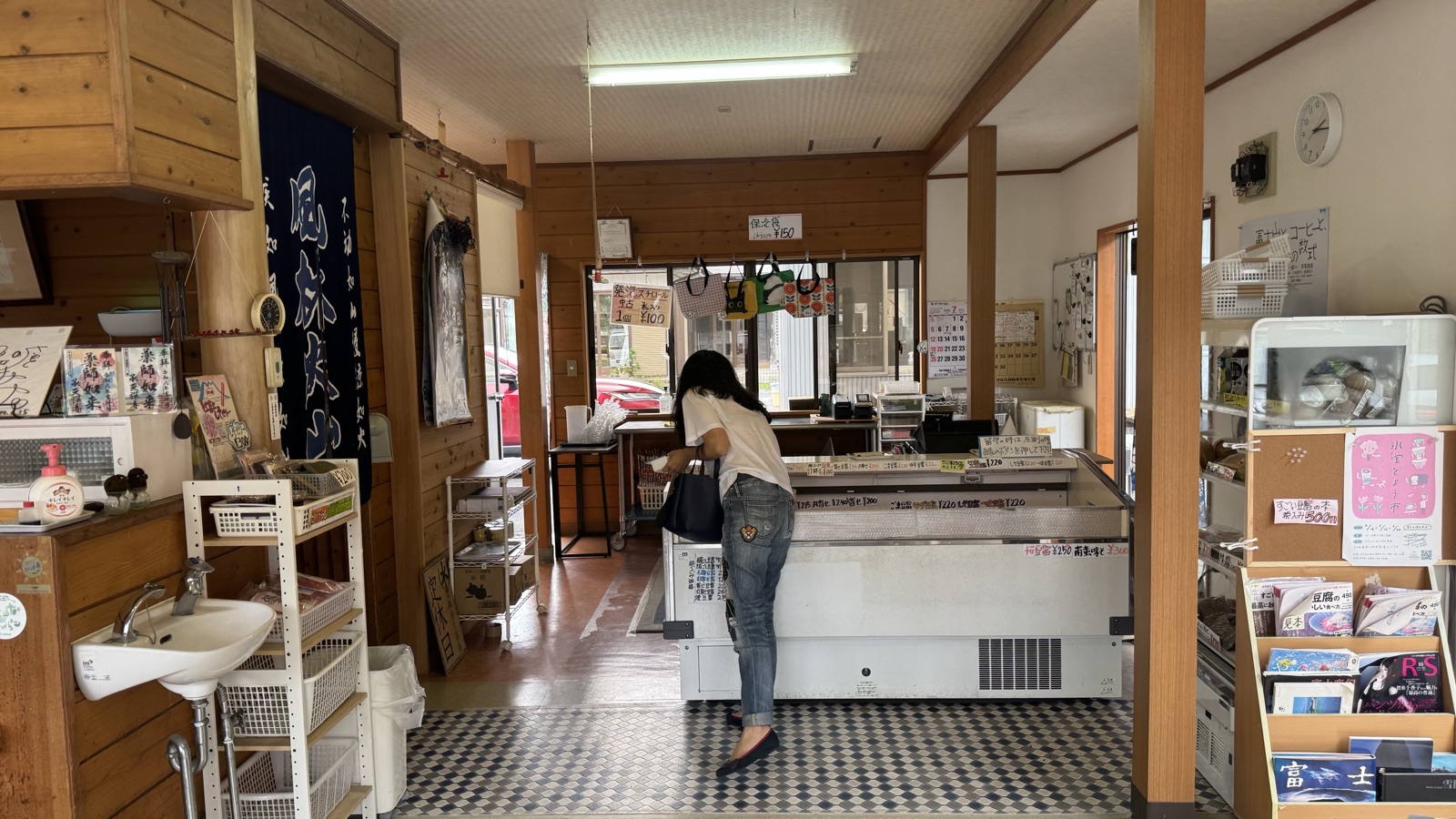 Inside Kadoya Tofu: a customer at the chilled case under an indigo Furin-Kazan curtain