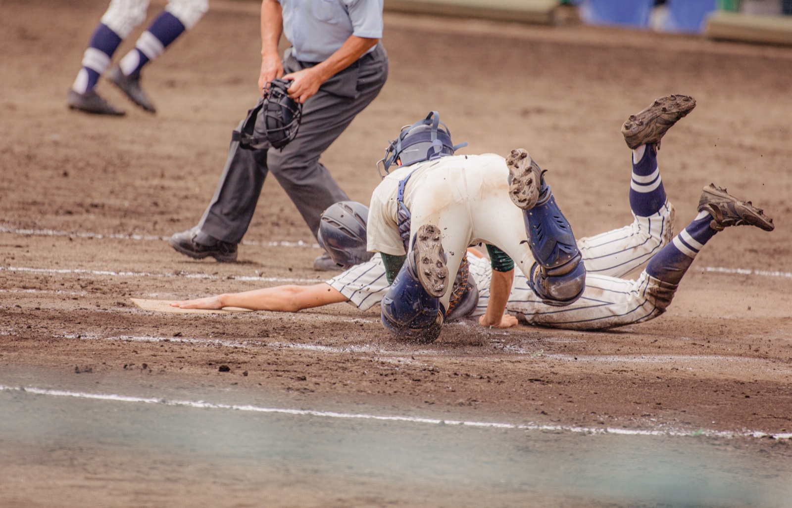 A runner and catcher converge at home plate as an umpire watches the play