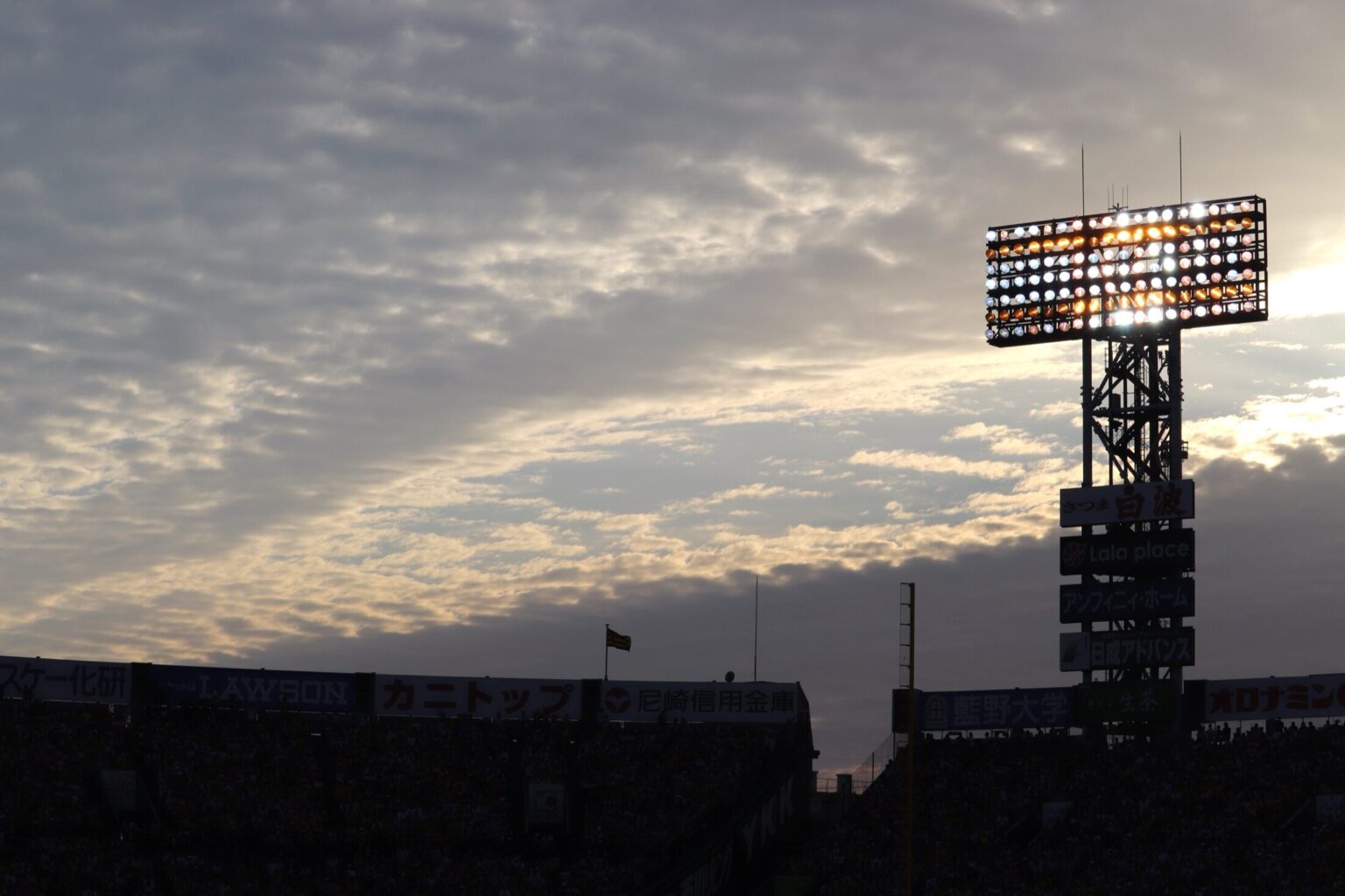 The floodlight tower of Hanshin Koshien Stadium silhouetted against a dramatic dusk sky above the stands