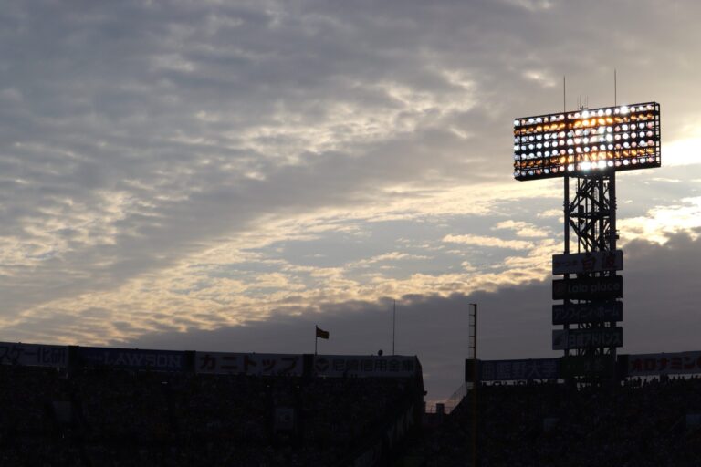 The floodlight tower of Hanshin Koshien Stadium silhouetted against a dramatic dusk sky above the stands