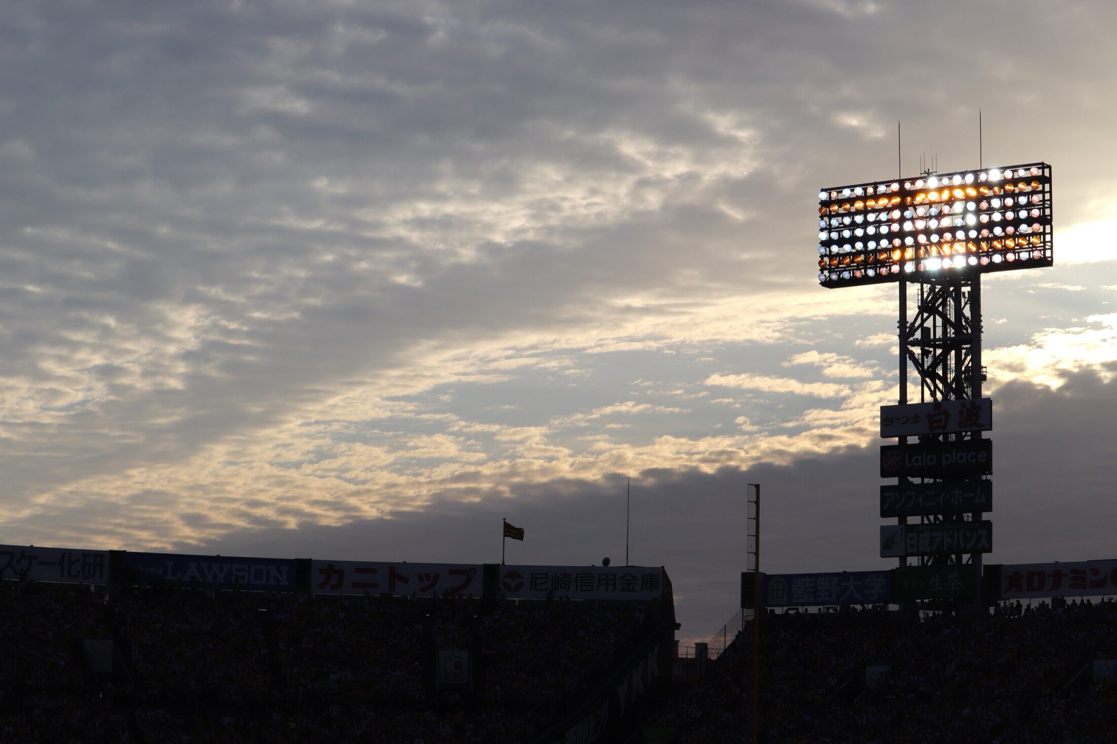 The floodlight tower of Hanshin Koshien Stadium silhouetted against a dramatic dusk sky above the stands