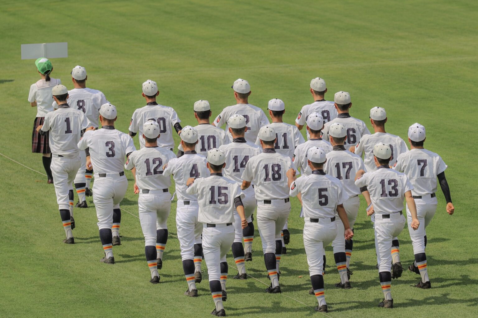 A high school baseball team jogging onto the field in numbered uniforms at Koshien