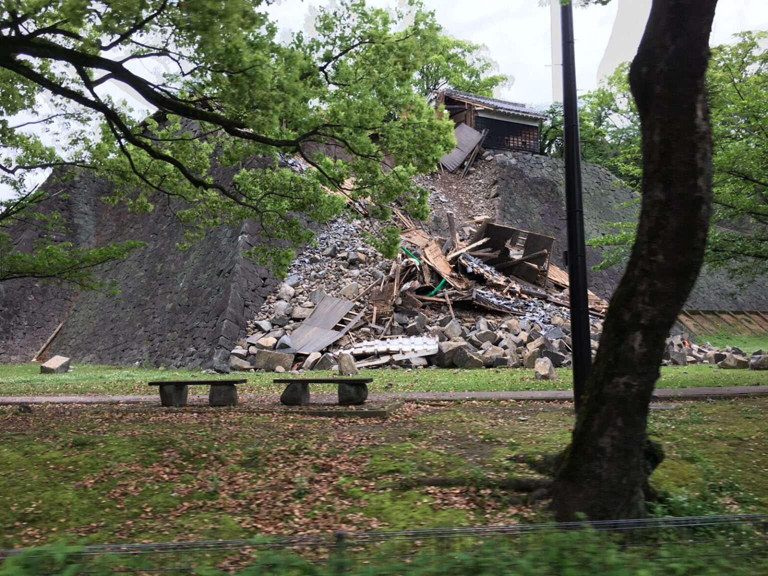 A collapsed stone wall and damaged turret of Kumamoto Castle seen through trees after the April 2016 earthquake, rubble piled at the base of the historic ramparts