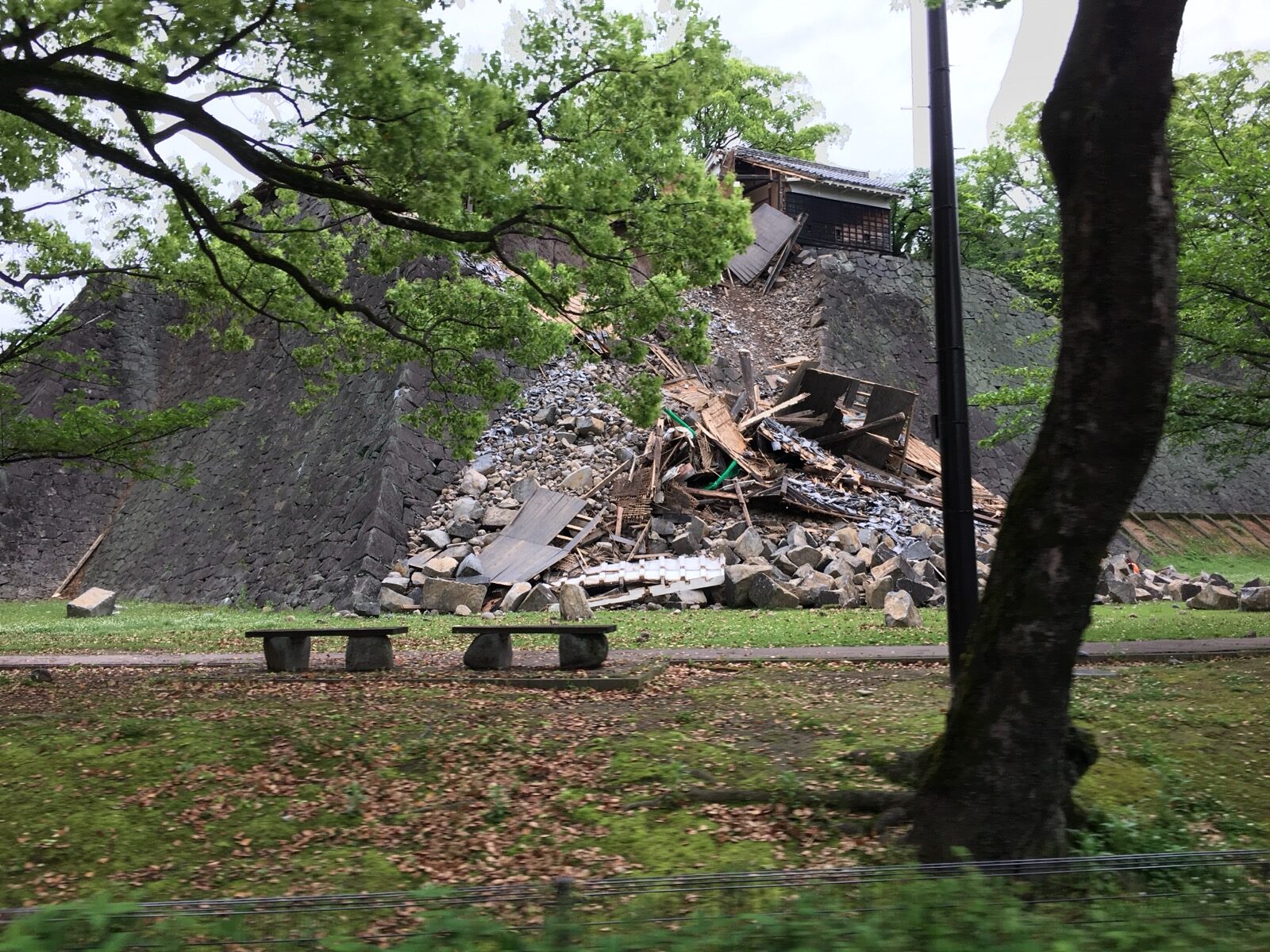 A collapsed stone wall and damaged turret of Kumamoto Castle seen through trees after the April 2016 earthquake, rubble piled at the base of the historic ramparts