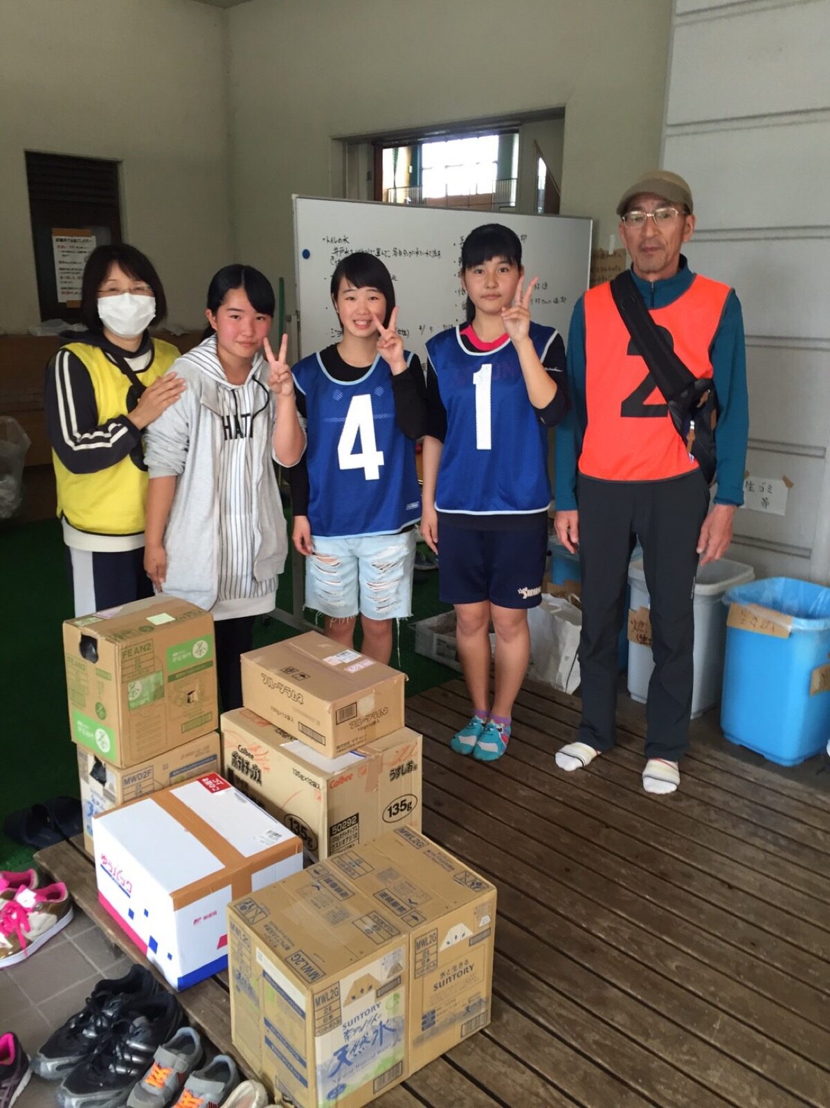 Young volunteers standing behind stacked cardboard boxes of relief supplies at an aid point after the April 2016 Kumamoto earthquake
